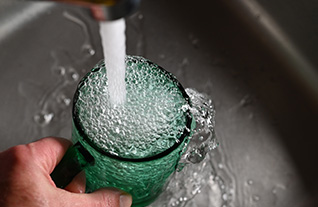 A hand holds a green cup overflowing with water from a faucet in a sink.